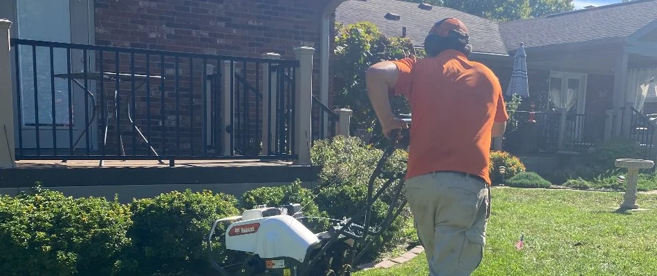 Gardener operating tiller in backyard with flowers in Louisville, KY.