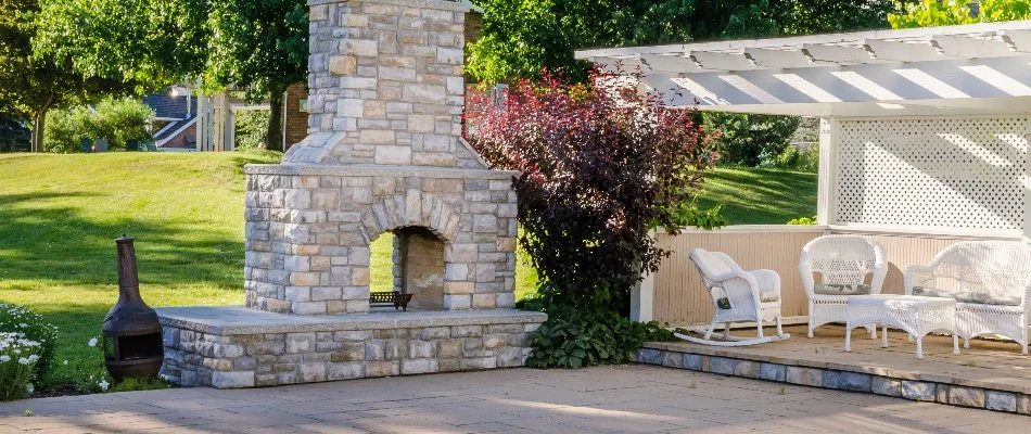 Outdoor fireplace in Louisville, KY, with white pergola and chairs.